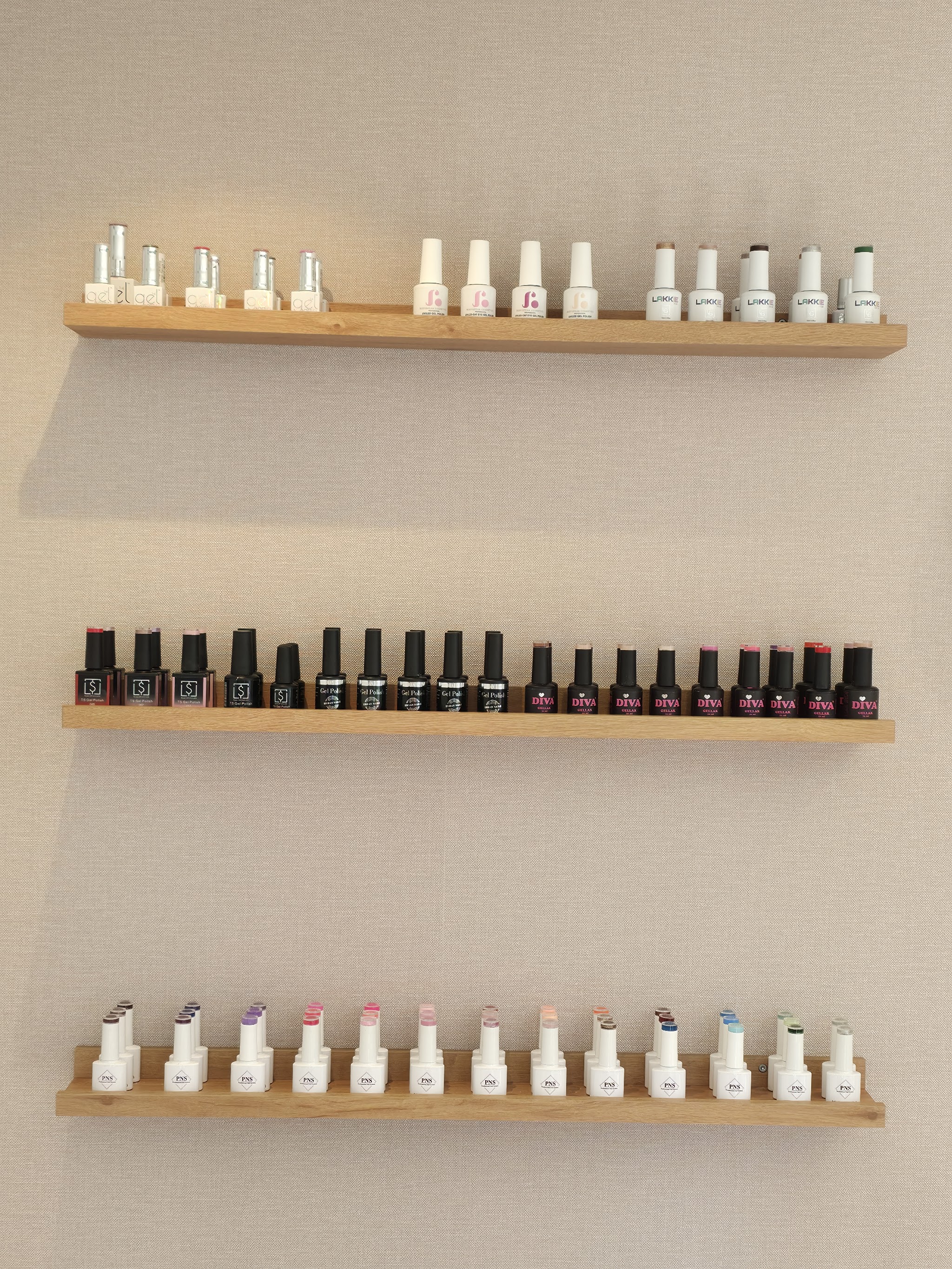 Drie houten planken vol gelpolish-flesjes aan de muur van de studio